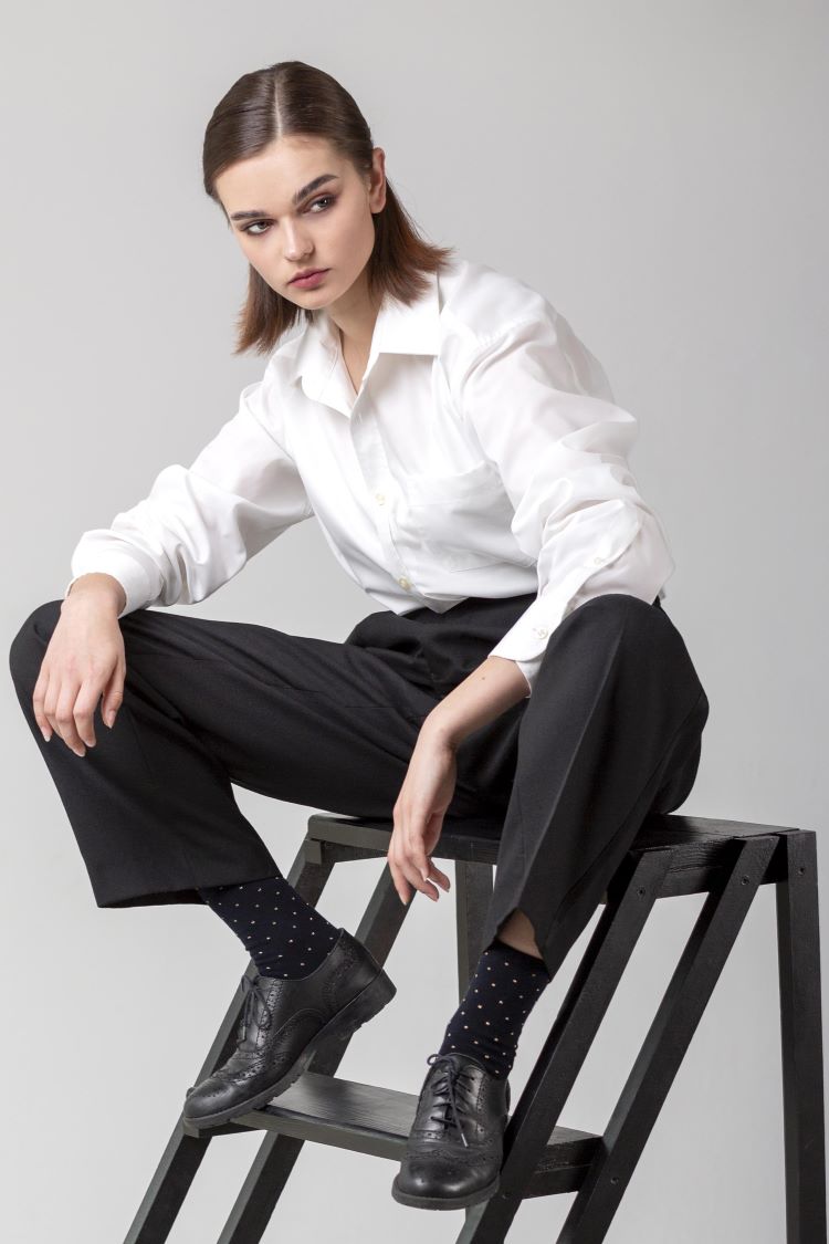 Lady in tailored black trousers, white shirt and black shiny shoes perches on a low step ladder