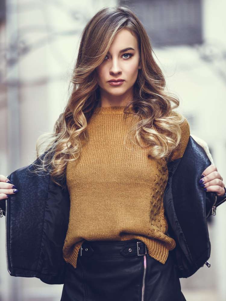 A lady wears a slim fitted mustard jumper under a zipped jacket with a pencil skirt.