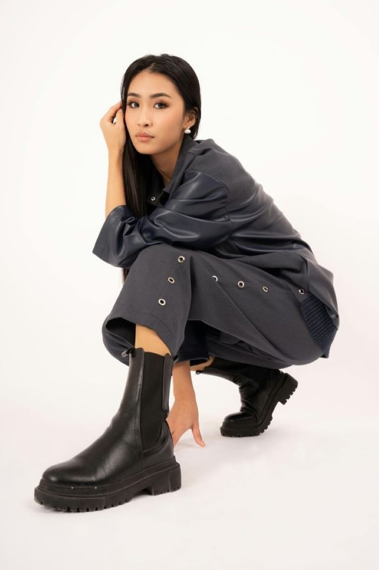 Crouching woman wearing grey trousers, long sleeve grey top and black chunky boots